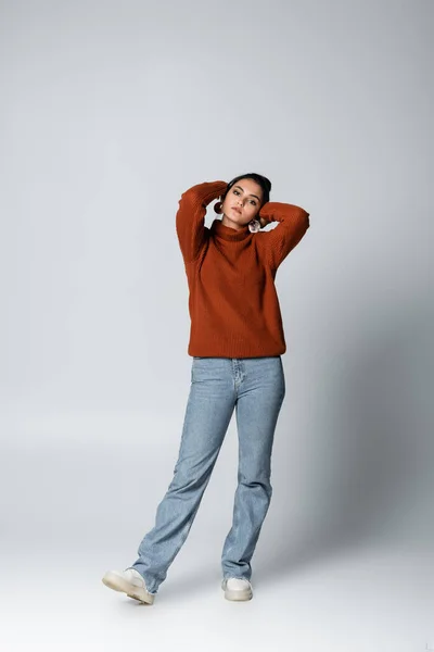 Full length of young woman in sweater and denim jeans posing on grey — Stock Photo