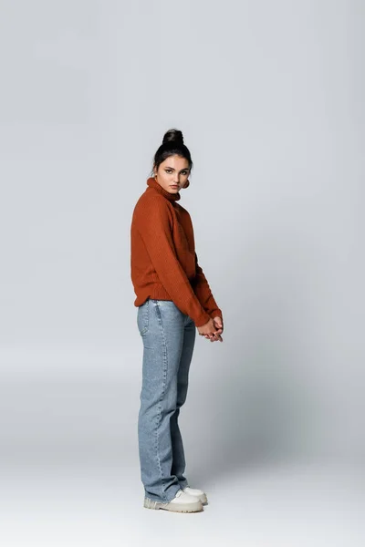 Full length of young model in sweater and denim jeans posing on grey — Stock Photo