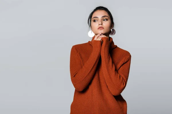 Mujer joven en suéter cálido mirando hacia otro lado aislado en gris - foto de stock