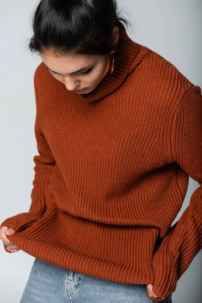 Giovane donna in orecchino guardando maglione lavorato a maglia isolato su grigio — Foto stock