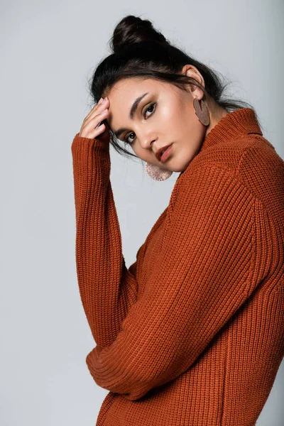 Young woman in earrings and knitted sweater looking at camera isolated on grey — Stock Photo