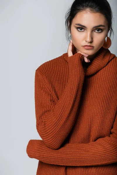 Young model in earrings and knitted sweater looking at camera isolated on grey — Stock Photo