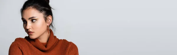 Jolie jeune femme en boucles d'oreilles et pull tricoté regardant loin isolé sur gris, bannière — Photo de stock