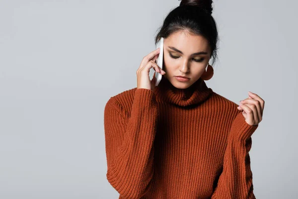 Jeune femme en pull tricoté parlant sur smartphone isolé sur gris — Photo de stock