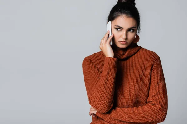 Giovane donna in maglione lavorato a maglia che parla sul cellulare isolato su grigio — Foto stock