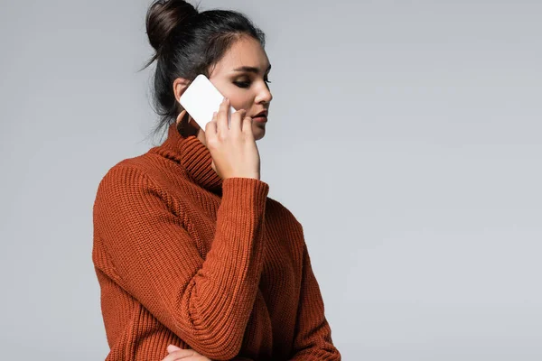 Молодая женщина в теплом свитере разговаривает на смартфоне изолированы на серый — стоковое фото