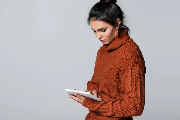 Giovane donna in maglione lavorato a maglia con tablet digitale isolato su grigio — Foto stock