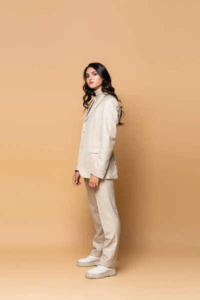 Pleine longueur de brunette jeune modèle en costume tendance sur beige — Photo de stock