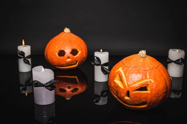 Brûlant des bougies près de citrouilles sculptées et effrayantes sur noir — Photo de stock