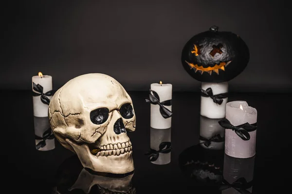 Skull near burning candles and carved pumpkin on black — Stock Photo