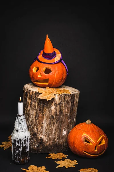 Creepy and carved pumpkin in pointed hat on wooden stump and black background — Stock Photo