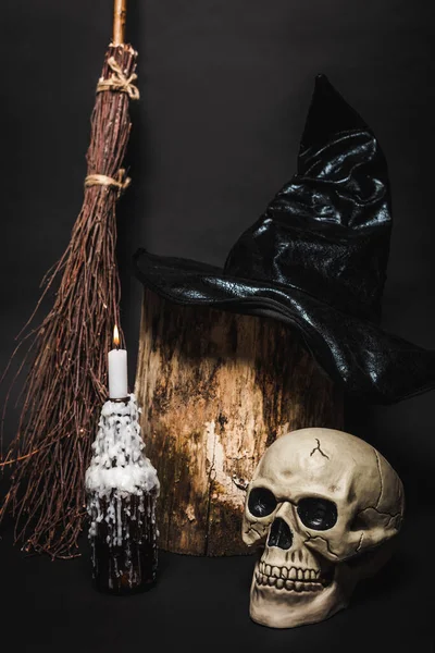 Broom near skull and wooden stump with witch hat on black — Stock Photo