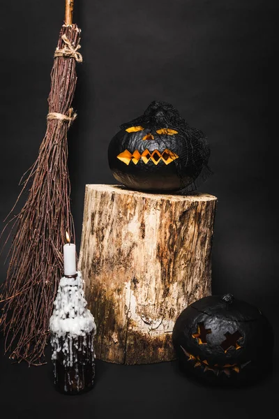 Broom near dark pumpkin on wooden stump near burning candle on black — Stock Photo