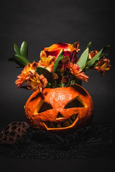 Orange flowers in spooky and carved pumpkin on black background — Stock Photo