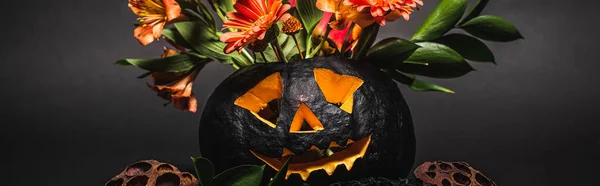 Orange flowers in spooky and carved pumpkin on black background, banner — Stock Photo