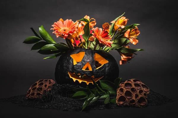 Orange flowers in spooky and carved dark pumpkin on black background — Stock Photo