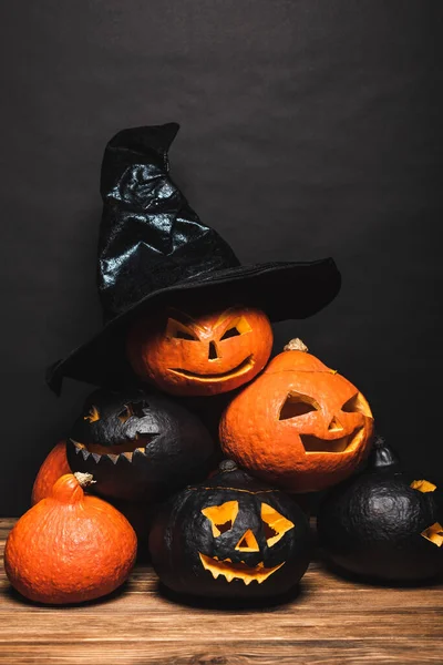 Stack of carved and creepy pumpkins with witch hat on top on black — Stock Photo