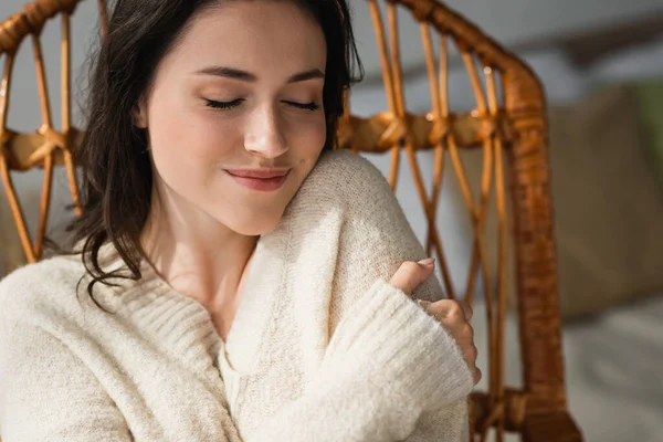 Zufriedene Frau im warmen Pullover, die sich zu Hause mit geschlossenen Augen umarmt — Stockfoto