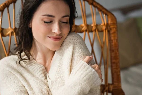 Femme heureuse en pull chaud se serrant dans ses bras tout en se reposant à la maison les yeux fermés — Photo de stock