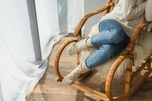 Обрезанный вид женщины в джинсах и теплых носках, сидящей в кресле-качалке — стоковое фото