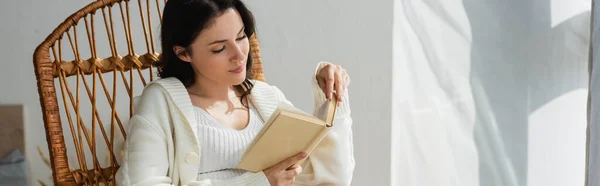 Молодая женщина в теплом кардигане чтение книги дома, баннер — стоковое фото