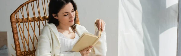 Mujer joven en un cálido libro de lectura de cárdigan en casa, pancarta - foto de stock