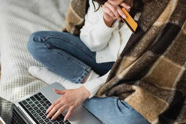 Cropped view of woman with credit card typing on laptop on bed — Stock Photo