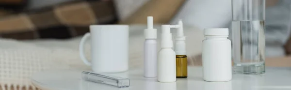 Botellas de spray y recipientes con medicamentos cerca del termómetro y bebidas en la mesa blanca, pancarta - foto de stock