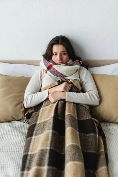 Kranke und aufgebrachte Frau schaut weg, während sie im Bett unter karierter Decke liegt — Stockfoto