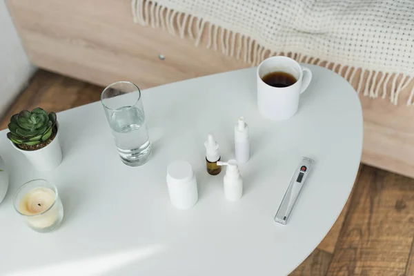 Vue grand angle des récipients et des bouteilles de pulvérisation avec des médicaments près des boissons et des plantes sur la table de chevet — Photo de stock