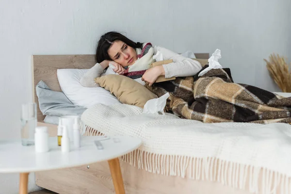 Femme malade couchée au lit sous une couverture à carreaux avec un paquet de serviettes en papier — Photo de stock