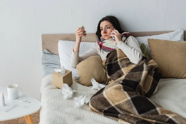 Sick woman with pills container talking on mobile phone while lying near crumpled paper napkins — Stock Photo