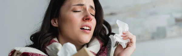 Femme malade tenant des serviettes en papier tout en éternuant avec les yeux fermés, bannière — Photo de stock