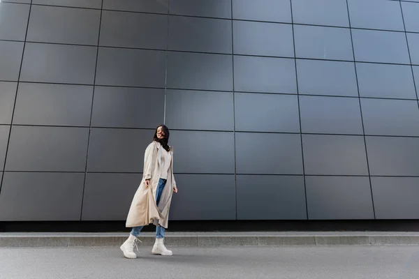 Стильна жінка в довгому пальто, озираючись назад, стоячи біля сірої стіни — стокове фото
