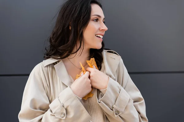 Trendige junge Frau schaut weg, während sie gelbe Blätter vor der Brust hält — Stockfoto