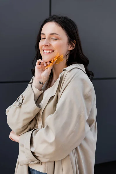 Pleased woman with closed eyes holding yellow leaves near face outdoors — Stock Photo