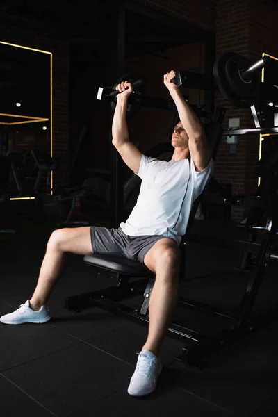 Vista completa del hombre en entrenamiento de ropa deportiva en la máquina de ejercicio de extensión de brazo - foto de stock