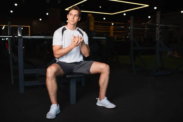 Visão de comprimento total do homem em sportswear sentado na máquina de exercício e aquecendo as mãos — Fotografia de Stock