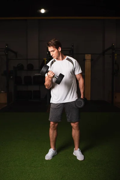 Vista completa del hombre en pantalones cortos haciendo ejercicio con pesas en el gimnasio - foto de stock