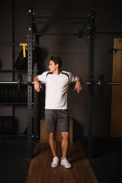 Vista completa del hombre en ropa deportiva de pie cerca de la máquina de ejercicios de levantamiento de pesas en el gimnasio - foto de stock
