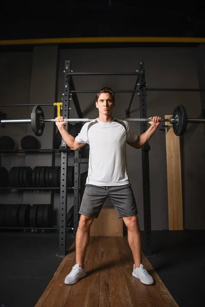 Vista completa del hombre en entrenamiento de ropa deportiva con barra de pesas en el gimnasio - foto de stock