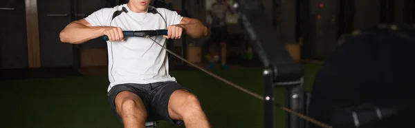 Vista recortada del deportista en pantalones cortos de entrenamiento en la máquina de ejercicios de cuerda de tracción, pancarta - foto de stock