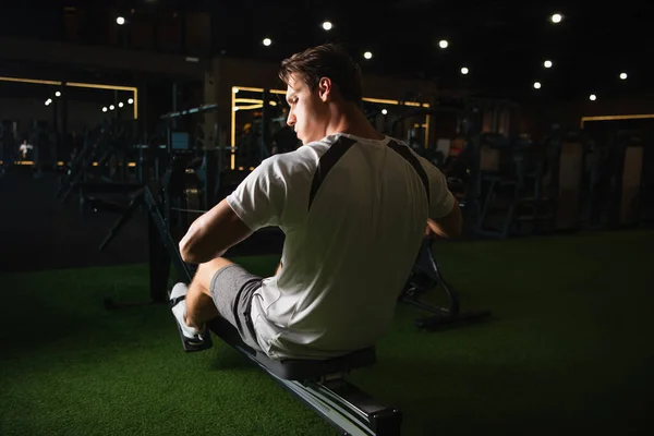 Vista posterior del entrenamiento del hombre en la máquina de ejercicios de cuerda de tracción en pose sentada - foto de stock