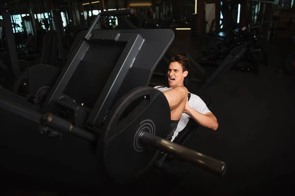 Desportista gritando enquanto trabalhava na extensão da perna exercitando máquina no centro de esportes — Fotografia de Stock