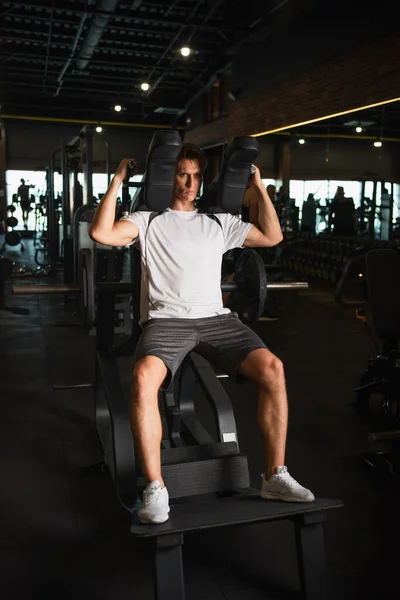 Full length view of sportsman training on arm extension exercising machine in gym — Stock Photo