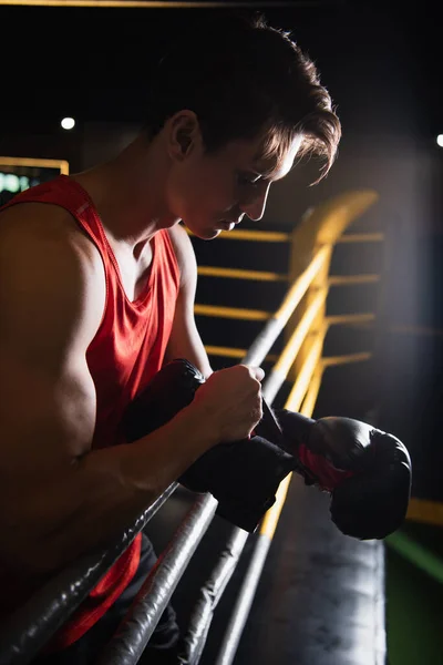 Boxer putting on gloves near ropes of boxing ring in sports center — Stock Photo