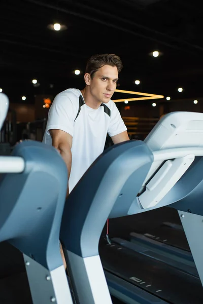 Homme sportif regardant loin tout en se tenant sur le tapis roulant dans la salle de gym — Photo de stock