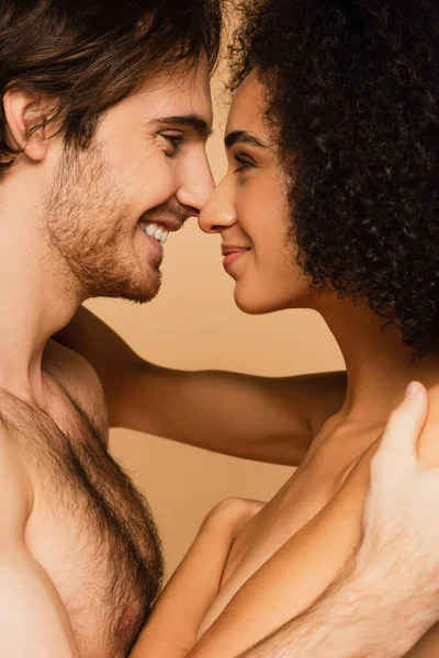 Vista lateral del hombre sin camisa y la mujer en topless sonriendo el uno al otro cara a cara aislado en beige - foto de stock