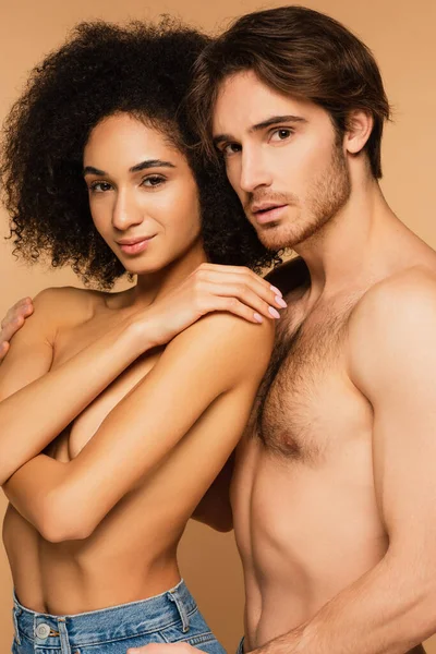 Sexy hombre sin camisa y seductora mujer hispana mirando a la cámara aislada en beige - foto de stock