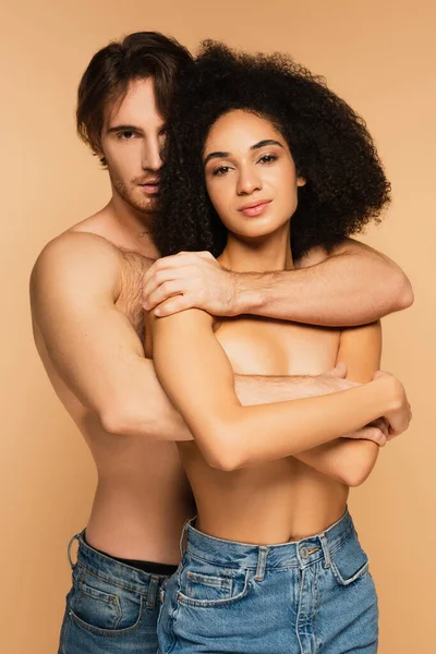 Sexy homem e topless latina mulher olhando para a câmera ao abraçar isolado no bege — Fotografia de Stock